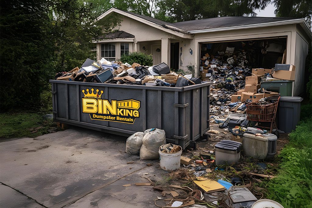 Bin King dumpster packed with junk and discarded items beside a cluttered home, used for downsizing and one-visit estate cleanouts.